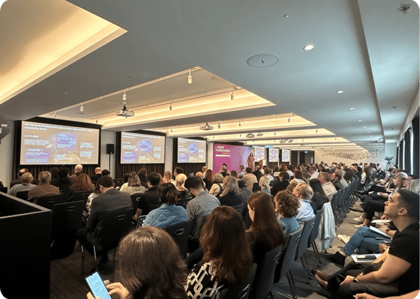 A seated audience watching a presentation displayed on screens in front of them